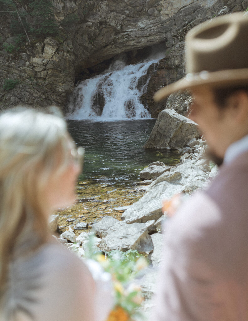 bride and groom at a waterfall before their logan pass elopement