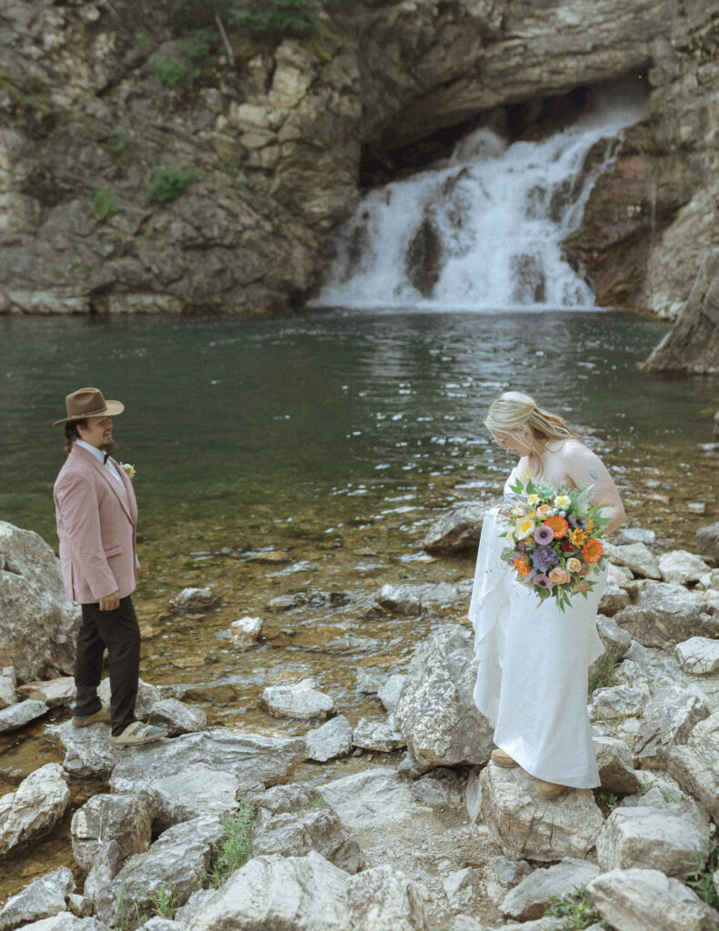 bride and groom at a waterfall before their logan pass elopement